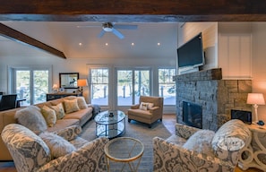 Cozy seating area with a fireplace, sofa, and armchairs, plus a flat-screen TV and large windows with outdoor views.