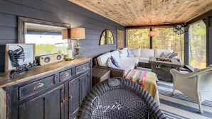 A cozy room with a wooden ceiling, a white sofa, a wicker chair, and a large mirror.