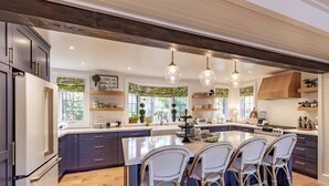 A modern kitchen with a large island, bar stools, pendant lighting, and a view of the outdoors.