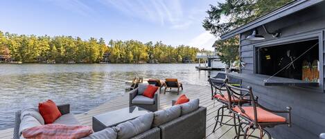 A waterfront deck with a sofa, chairs, and a bar area.