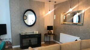 A living room with a beige sofa, a round mirror, pendant lights, a small table with a lamp, and a radiator. - 15% Off 4 Night Stays | Boutique 1 Bed Apartment (Cardiff)