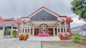 A building with a red and white facade, large windows, and a central entrance with a pink table. - OYO 3277 Inayah Pkpri Hotel Syariah (Serang)