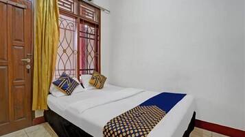 A room with a bed, a curtain, a window with a metal grille, and an air conditioning unit.