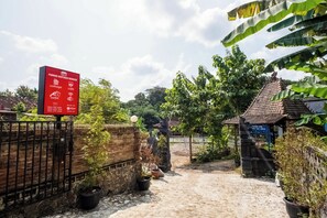 Un letrero muestra servicios como una cabaña, un café y un lugar para selfies, además de un camino que lleva a un edificio con tejado de tejas.