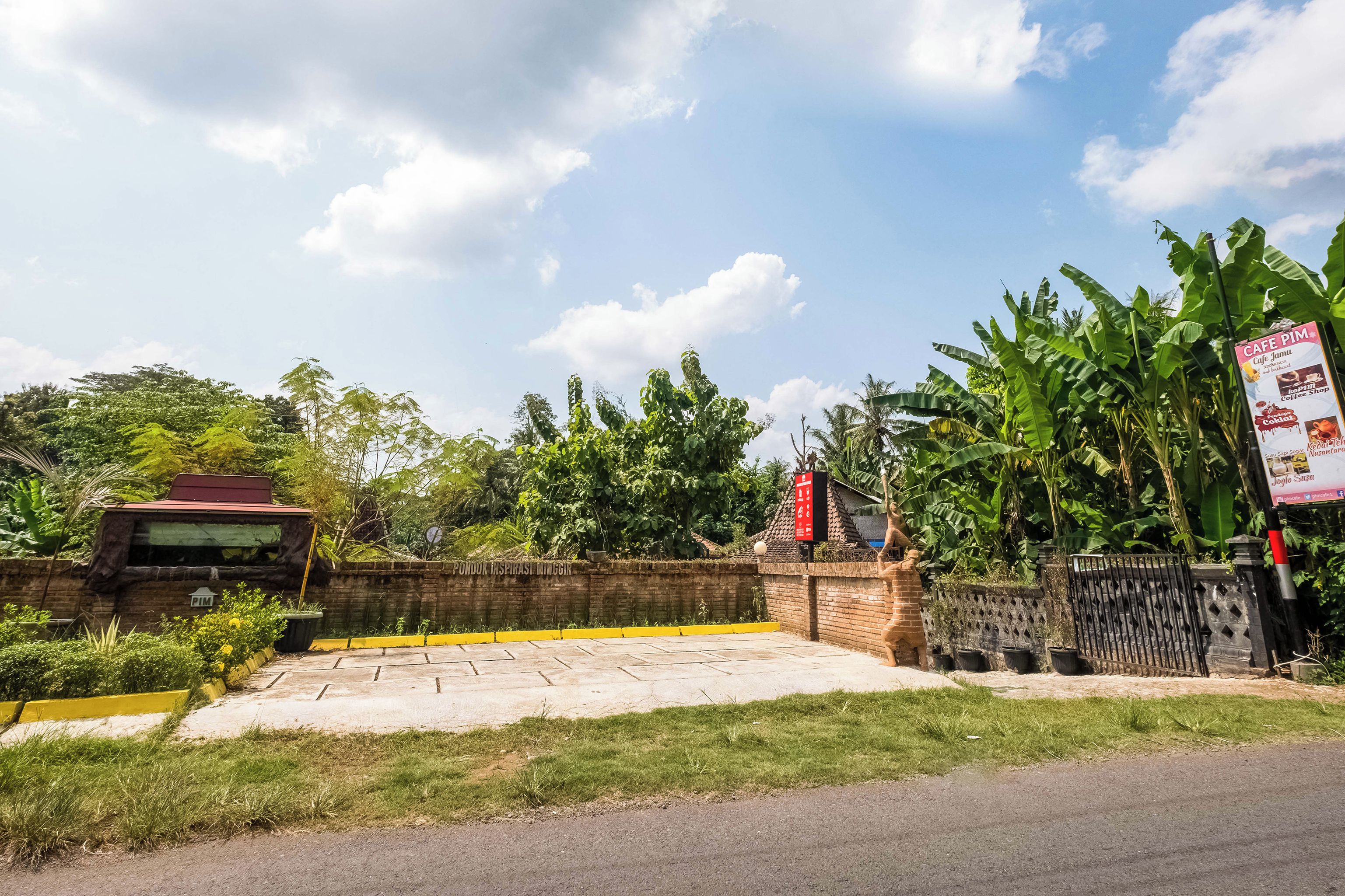 A gated entrance with a signboard, a paved area, and lush greenery.