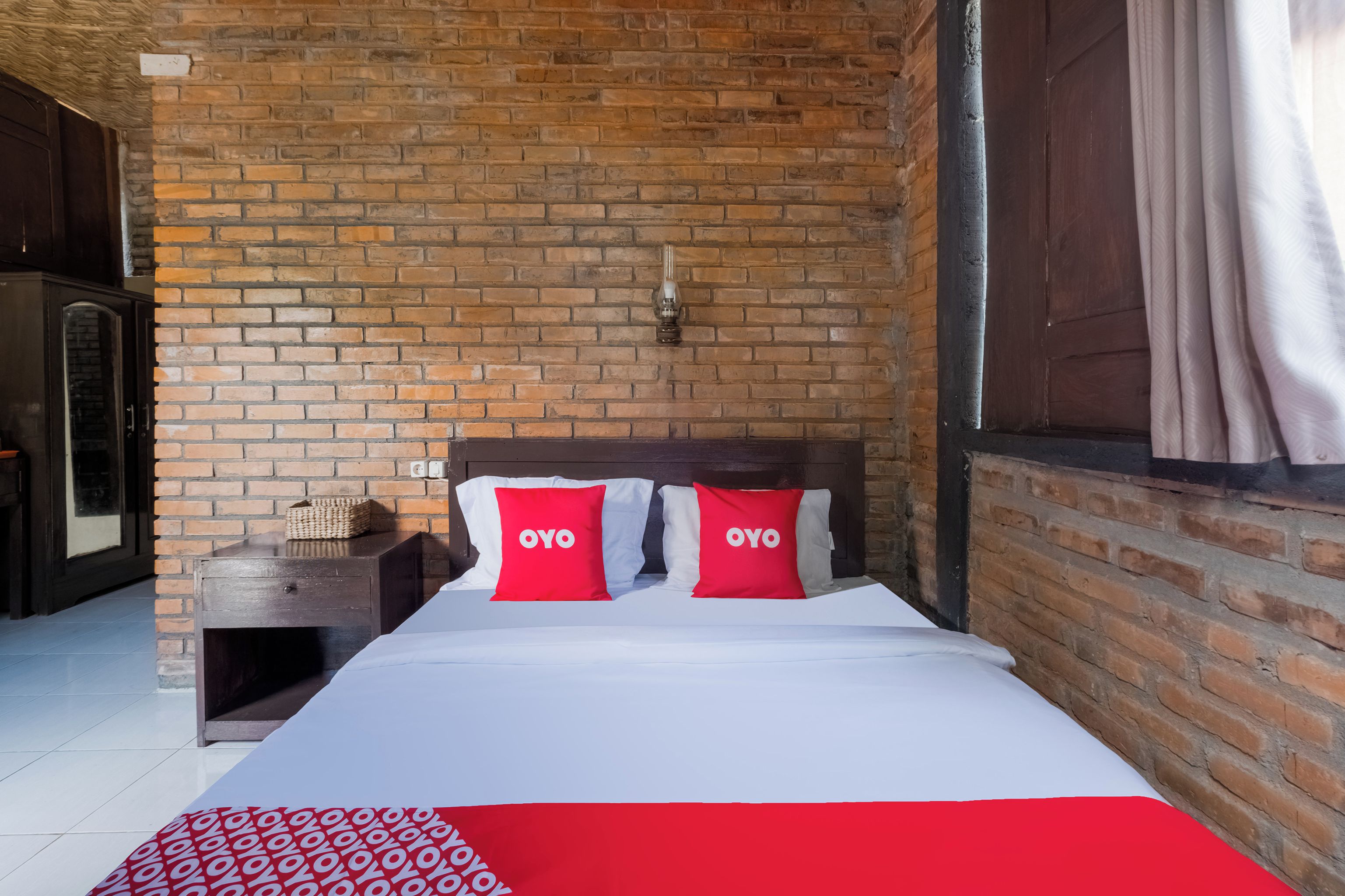 A hotel room with a brick wall, a wooden headboard, and a bed with red and white bedding.