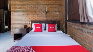Habitación de hotel con pared de ladrillo, cabecera de madera y ropa de cama roja y blanca.