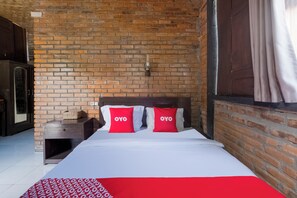Habitación de hotel con pared de ladrillo, cabecera de madera y ropa de cama roja y blanca.