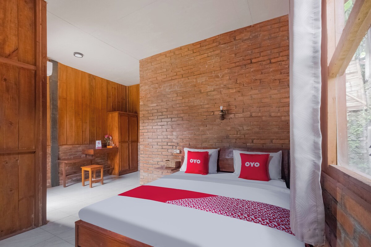 Un dormitorio con pared de ladrillo, muebles de madera, cama con ropa de cama roja y blanca, y ventana con vistas.