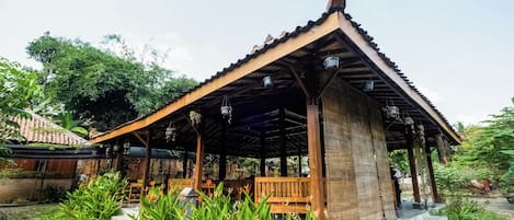 A wooden pavilion with a tiled roof, surrounded by lush greenery and stone steps leading to seating areas.