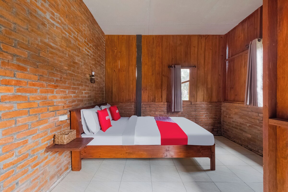 Un dormitorio con cama de madera, paredes de ladrillo y ventana con cortinas.