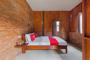 Ein Zimmer mit Backsteinwand, Holzvertäfelung, einem Bett mit weißer Bettwäsche und roten Kissen, einem Nachttisch und einem Fenster mit Vorhängen.