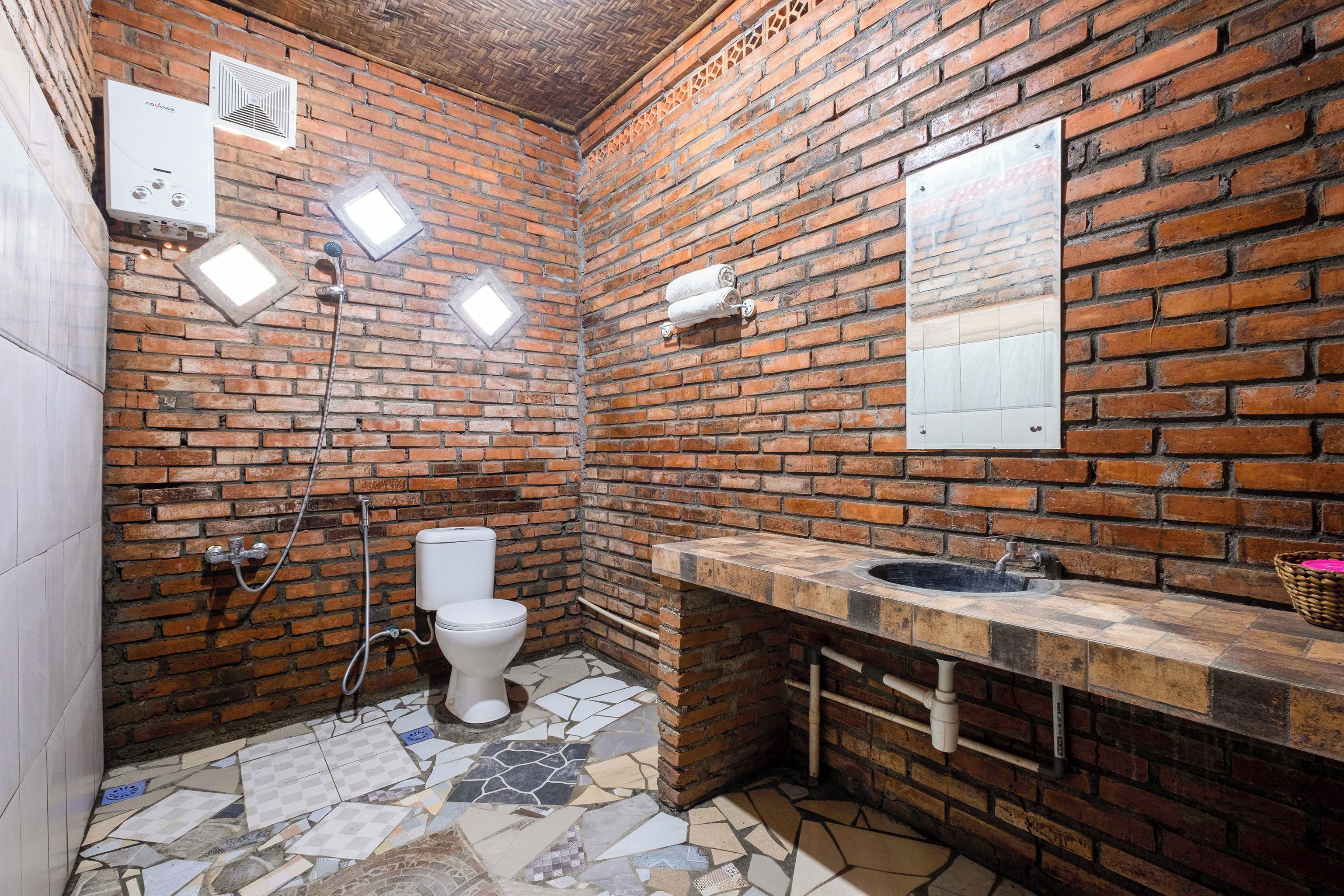 Un baño con pared de ladrillo, inodoro blanco, lavabo con encimera de piedra y zona de ducha.
