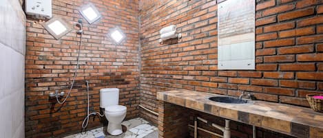 Une salle de bain avec un mur en briques, des toilettes blanches, un lavabo avec un plan de travail en pierre et un espace douche.
