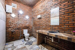 Un baño con pared de ladrillo, inodoro blanco, lavabo con encimera de piedra y zona de ducha.