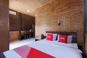 Una habitación de hotel con pared de ladrillo, una cama con ropa de cama roja y blanca, y una mesita con un florero.