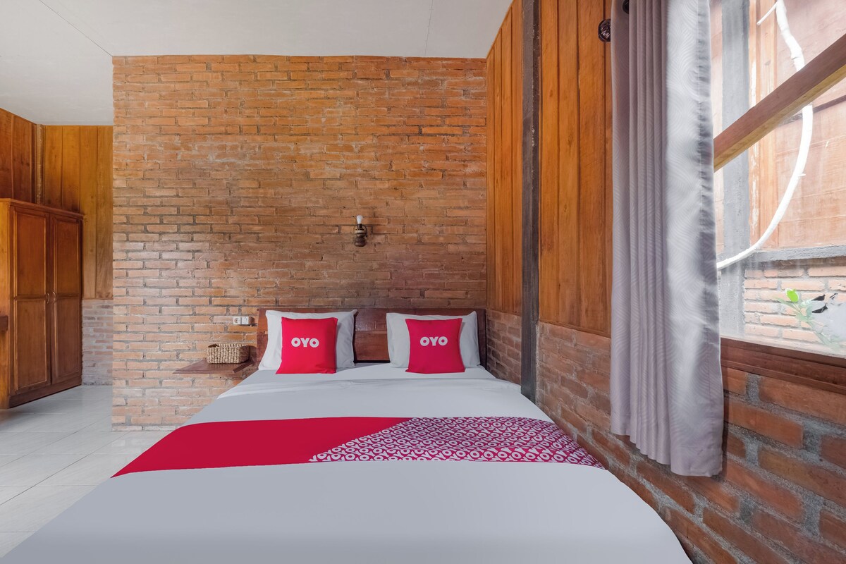 Habitación de hotel con pared de ladrillo, armario de madera y cama con ropa de cama roja y blanca.