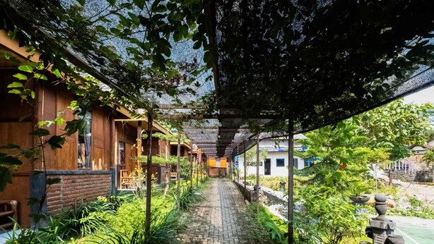 A covered pathway lined with greenery and traditional architecture, leading to a building with wooden walls and a thatched roof. - OYO 3562 Pondok Inspirasi Minggir (Minggir)