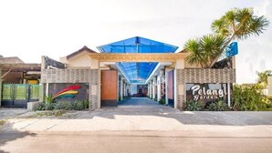 Une entrée moderne avec un toit de verre, une enseigne indiquant « Pelangi Garden » et un logo coloré sur le côté gauche.