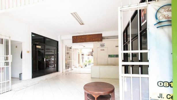 A spacious indoor area with a round wooden table, a sign above a doorway, and a glass door with a metal frame. - Spot ON 3961 Fico's Residence Syariah (Bekasi)
