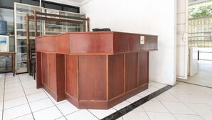A wooden reception desk in a room with tiled flooring and a glass door in the background. - Spot ON 3961 Fico's Residence Syariah (Bekasi)