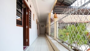 A corridor with a tiled floor, a metal fence, and a view of a tiled roof and greenery outside. - Spot ON 3961 Fico's Residence Syariah (Bekasi)