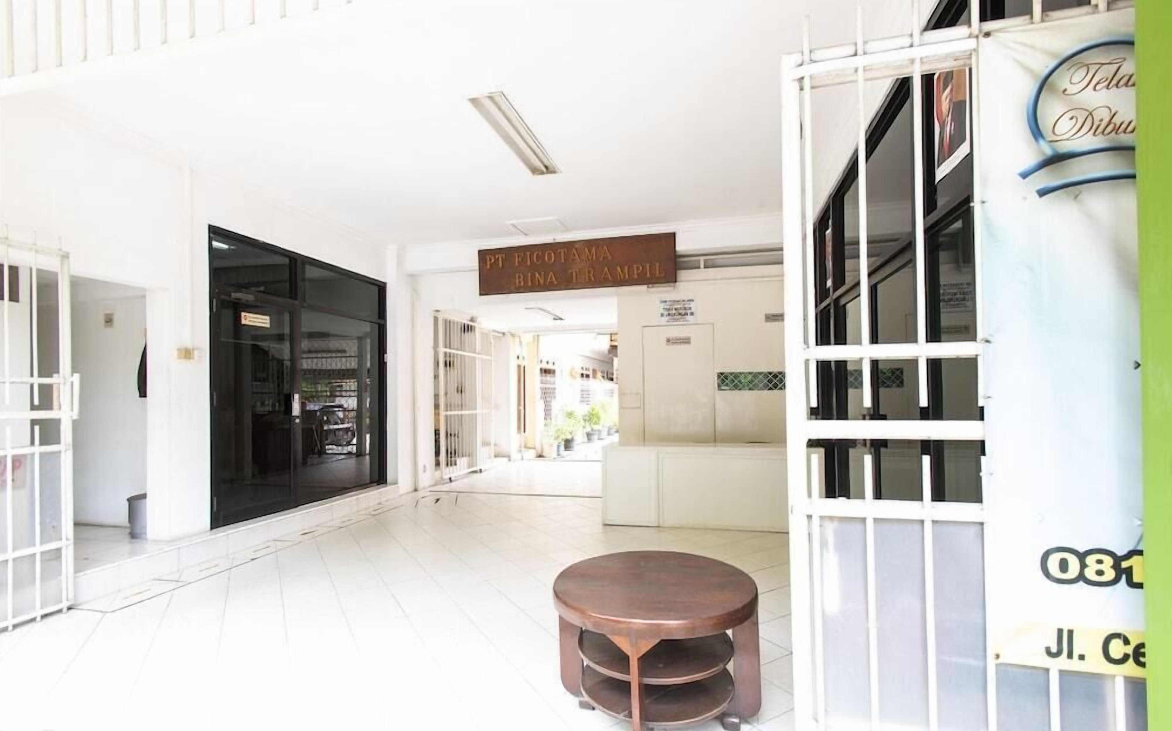 Un espacio interior amplio con un gran ventanal que da a un pasillo, una mesa redonda de madera, y un cartel sobre la puerta.