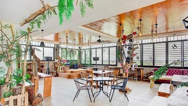 Un vaste espace intérieur aménagé avec des meubles en bois, une scène et des plantes suspendues.