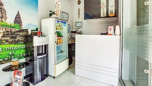 A hotel room with a minibar, a refrigerator stocked with beverages, a small table with a vase of flowers, and a mural of a temple on the wall. - OYO 3338 Wisma Anugerah Syariah (Surakarta)
