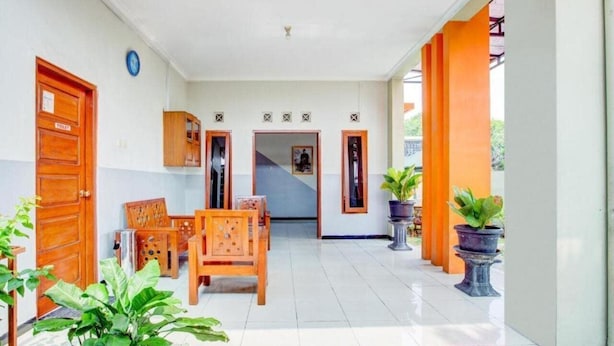 A clean, well-lit hallway with wooden doors, a seating area with a table and chairs, and potted plants. - OYO 3338 Wisma Anugerah Syariah (Surakarta)