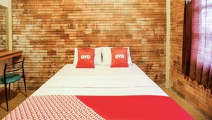 Een hotelkamer met een met baksteenpatroon betegelde muur, een bed met twee kussens, een bureau en een stoel.