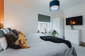 A modern bedroom with a large bed, a TV, a wardrobe, and a window with a view of buildings. - Entire House with Parking in Rugby (Rugby)