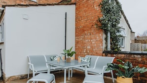 A patio with a glass table and white chairs, surrounded by a brick wall and a white door. - Entire House with Parking in Rugby (Rugby)