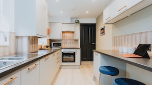 A modern kitchen with white cabinets, a microwave, an oven, and a dark door. There are two blue bar stools and a laptop on the counter. - Entire House with Parking in Rugby (Rugby)