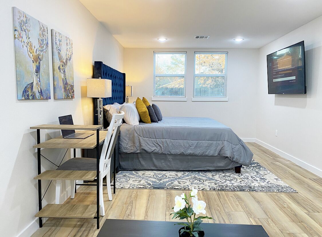 A modern bedroom with a bed, a desk, a chair, a TV, and artwork on the wall.
