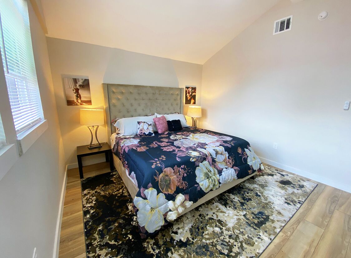 A bedroom with a large bed, two bedside tables, a headboard, and two wall-mounted lamps.