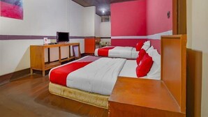 Ein Hotelzimmer mit zwei Betten, einem Schreibtisch mit Computer und einer roten und weißen Farbgestaltung.