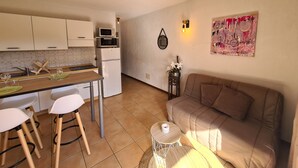 Un espacio habitable compacto con kitchenette, una zona de comedor con taburetes, un sofá y una mesita auxiliar.