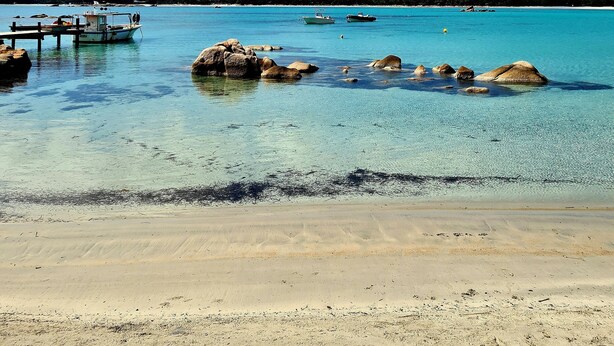 Una playa con aguas turquesas cristalinas, rocas y barcos.