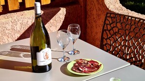 Una mesa con una botella de vino, dos copas, un plato de carne y un bol de fruta.