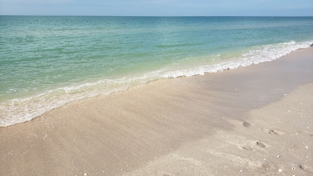 Una playa con agua turquesa cristalina, una orilla arenosa y huellas en la arena.