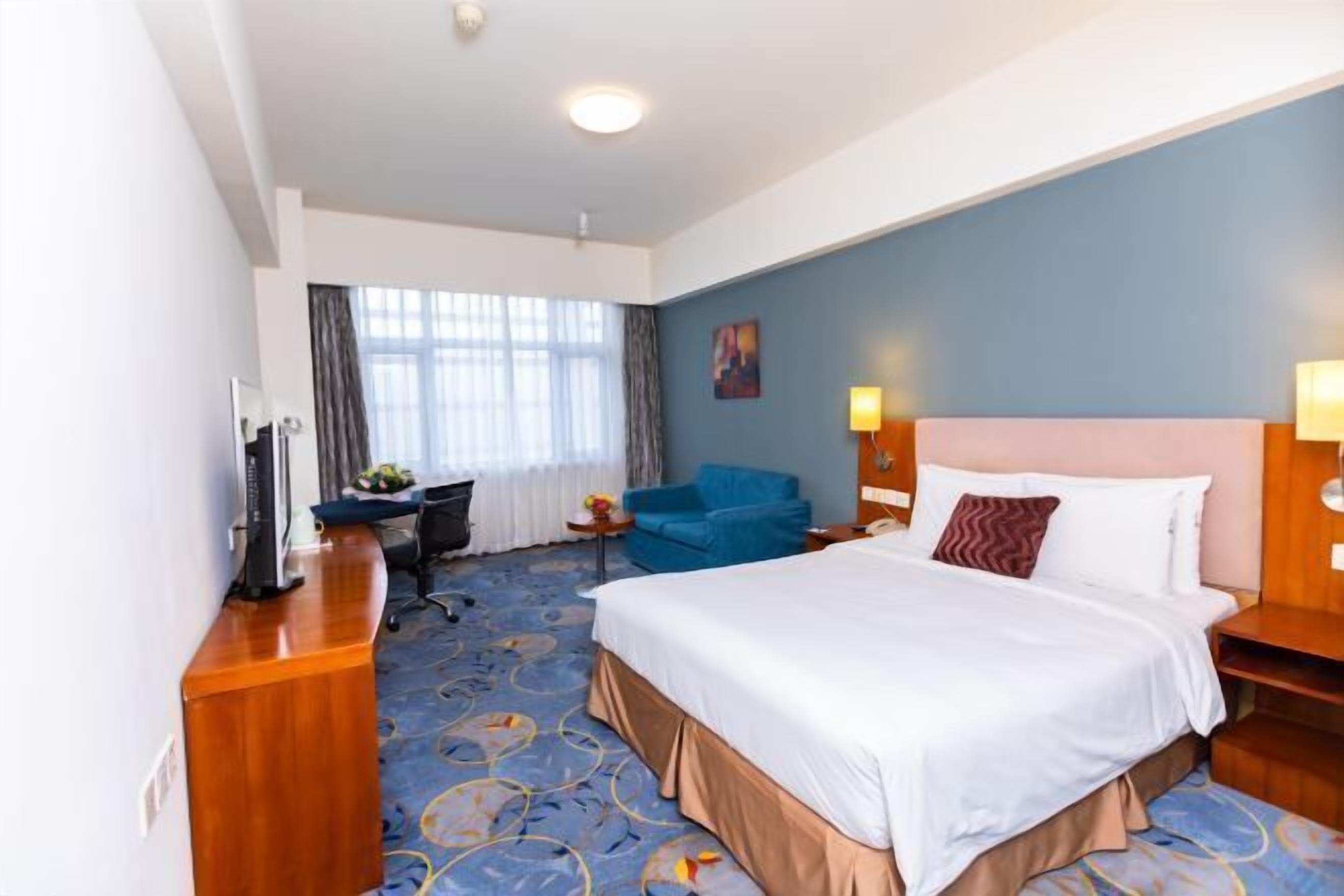 Una habitación de hotel con una cama grande, un escritorio, una silla y una pared azul.