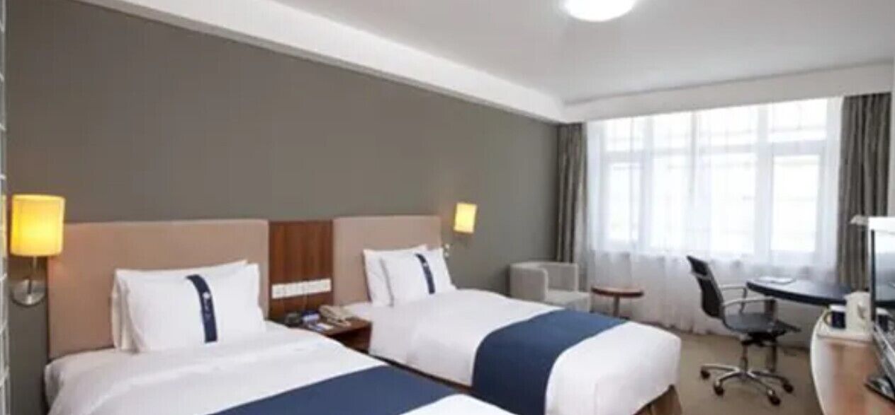 A hotel room with two beds, a desk, a chair, and a large window.