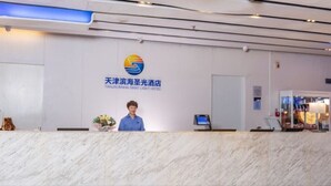 A hotel reception desk with a logo, a receptionist, and a computer monitor. - Tianjin Binhai Saint Light Hotel (Tianjin)
