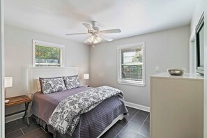 Un dormitorio con una cama, lámparas de noche, un ventilador de techo y ventanas con persianas.