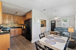 A modern kitchen with wooden cabinets, a black refrigerator, and a dining area with a table and chairs. - Beachy Isle of Palms Private Bungalow! Walk to Beach! Pet Friendly. (Isle of Palms)