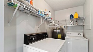 A laundry room with a Kenmore washer and dryer, a Rheem water heater, and shelves with cleaning supplies. - Beachy Isle of Palms Private Bungalow! Walk to Beach! Pet Friendly. (Isle of Palms)