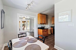 A modern kitchen with wooden cabinets, a dining area with a table and chairs, and a view of a patio with outdoor seating. - Beachy Isle of Palms Private Bungalow! Walk to Beach! Pet Friendly. (Isle of Palms)