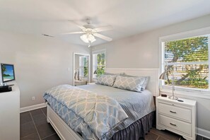 A bedroom with a bed, a nightstand, a desk, a ceiling fan, and a window with blinds. - Beachy Isle of Palms Private Bungalow! Walk to Beach! Pet Friendly. (Isle of Palms)