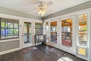 Una habitación con ventilador de techo, puerta corrediza de vidrio que da a un espacio exterior y una mesita con cajones.